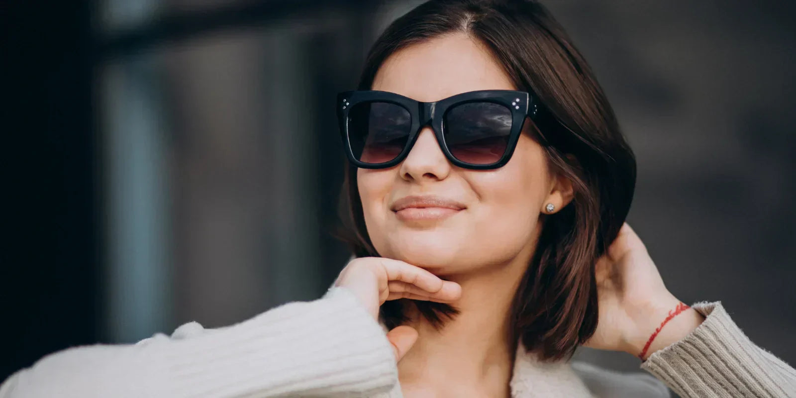 Stylish woman in light summer wear with elegant sunglasses and earrings, set against a soft, blurred background